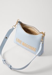 Svetlo modra napa usnjena torba čez ramo z zlatim napisom "LOVE MOSCHINO", zadrgo in nastavljivim trakom. Notranjost je bež.