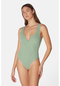 Grön ruggad baddräkt med djup V-ringning och breda axelband, med en texturerad tyg och högskurna benöppningar.