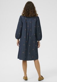 Das Jeanskleid zeichnet sich durch eine dunkelblaue Farbe, Voyagenärmel und ein knielanges Design mit verstreuten braunen Schmetterlingsstickereien aus.