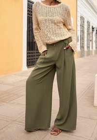 Pull en tricot crème avec un motif à mailles ouvertes, associé à un pantalon large olive décontracté avec deux boutons à l'avant et de profondes poches.