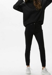 Black oversized hoodie with a drawstring, paired with black slim-fit pants and white sneakers. Smooth fabric, minimalistic design.