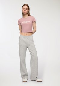 T-shirt corto rosa chiaro con testo bianco. Pantaloni sportivi grigi larghi. Tessuto morbido con una consistenza soffice e cintura elastica.