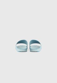 Chaussons bleus à glissière avec un design ouvert, fabriqués en plastique lisse, présentant une semelle plate et une silhouette minimaliste. Pas de motifs ni d'accents.