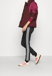 Maroon and purple jacket with zipper; black pants with white side stripes; beige and pink sneakers; textured fabric and athletic design.