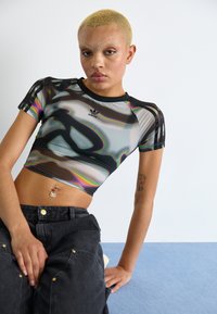 Black mesh cropped T-shirt with abstract iridescent patterns, short sleeves, and a round neckline. Paired with dark high-waisted cargo pants.