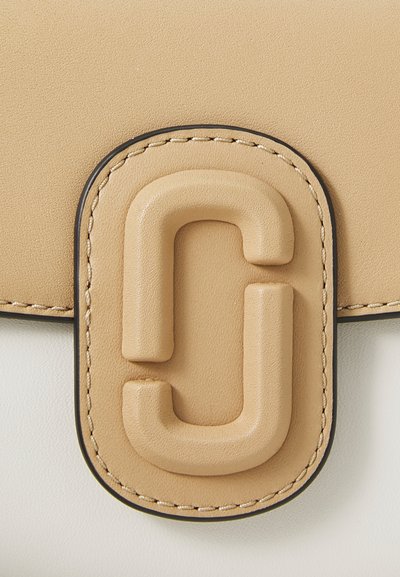 Tan leather closure featuring a raised, embossed logo, stitched edges, and a textured finish against a smooth white background.