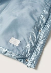 Světle modrý zateplený kabát uvnitř, s lesklou tkaninou, jednoduchou bílou etiketou a stříbrnými patentními knoflíky.