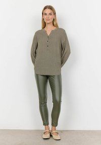 Khaki patterned blouse with a V-neck and three buttons, paired with olive green fitted pants and beige slip-on shoes. Smooth fabric texture.