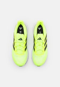 Baskets de sport d'un jaune néon éclatant avec des accents noirs, tige en mesh texturé et semelles en caoutchouc blanches. Comprend des lacets réglables et un logo.