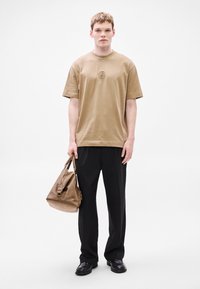 Χακί βαμβακερό μπλουζάκι με κοντά μανίκια, στρογγυλή λαιμόκοψη και κεντητό λογότυπο. Συνδυασμένο με μαύρο παντελόνι και καφέ δερμάτινη τσάντα.