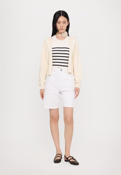 Biele šortky v kombinácii s krémovým skráteným kardigánom a pruhovaným čierno-bielym topom. Hnedé sandále so strapcami dopĺňajú outfit.