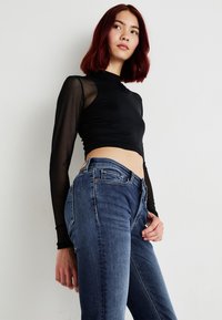 Zwarte lange mouwen crop top met sheer mesh mouwen, gecombineerd met donkerblauwe denimjeans met een klassieke pasvorm en zichtbare stikdetails.