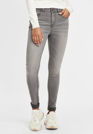 Jeans de denim gris ajustados con una textura desteñida, diseño de cinco bolsillos y puños enrollados, combinados con zapatillas de color claro.