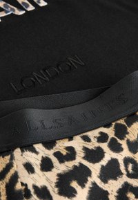 Svart topp med präglad text "LONDON", i kombination med ett leopardmönstrat textilmaterial. En svart elastisk remsa har texten "ALLSAINTS".