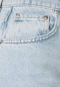 Ljust tvättade denimjeans med en bakficka med en silverknapp, synlig söm och en mjuk, texturerad tygfinish.