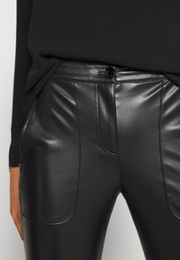 Pantaloni in pelle nera con una texture liscia, design aderente e cuciture a contrasto. Inclusi tasche frontali funzionali e chiusura con bottone.