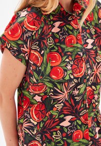 Chemise à manches courtes avec boutons, présentant un motif floral orange vif sur fond noir, fabriquée en tissu léger.