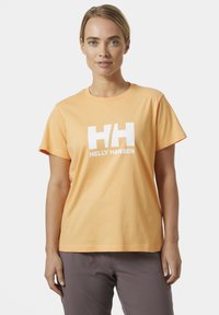 Camiseta de algodón naranja con mangas cortas, escote redondo, que presenta un gran logo blanco de "HELly HANSEN" en el frente. Corte estándar.