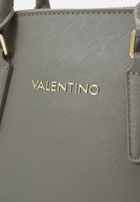 Szara torebka o teksturowanym wykończeniu, ze złotymi akcentami i wyraźnie wyeksponowanym logo "VALENTINO" z przodu.