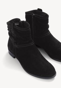 Bottines en daim noir avec fermetures éclair latérales, talons bas et surpiqûres décoratives autour de la cheville et des orteils.