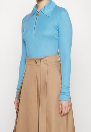 Jasnoniebieski longsleeve z kołnierzem na zamek oraz beżowa spódnica z wysokim stanem, zapinana na guziki, z bocznymi kieszeniami.