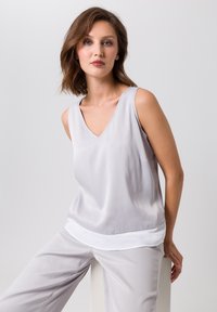 Helles graues, ärmelloses Oberteil mit V-Ausschnitt und weißem Saum. Aus glattem Stoff gefertigt, mit entspanntem Schnitt und dezentem Glanz.