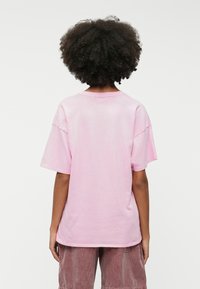 Light pink oversized t-shirt with short sleeves, round neckline, and a smooth cotton texture, viewed from the back.