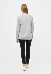 Grauer Pullover mit Rundhalsausschnitt, gerippten Bündchen und Saum. Kombiniert mit schwarzen Slim-Fit-Jeans und weißen Sneakers. Glatte Textur.