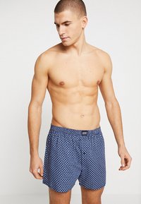 Blå mönstrade kalsonger i mjuk bomull, med knapflytt och elastisk midja med en märkesetikett.