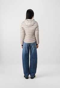 Helle beige Daunenjacke mit Kapuze und gesteppten Details. Kombiniert mit locker sitzenden blauen Jeans. Schwarze Schuhe.