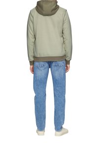 Khaki hoodie met een bicolor ontwerp, gecombineerd met lichtblauwe denim jeans. De hoodie heeft een trekkoord en ribgebreide manchetten.