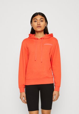 Sweat à capuche corail avec cordons, présentant des poignets et un ourlet côtelés, associé à un short noir ajusté. Détail de logo simple sur la poitrine.