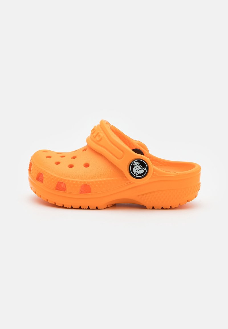 Sabot orange vif avec des trous de ventilation et une bride de talon réglable avec un logo circulaire noir sur fond blanc.