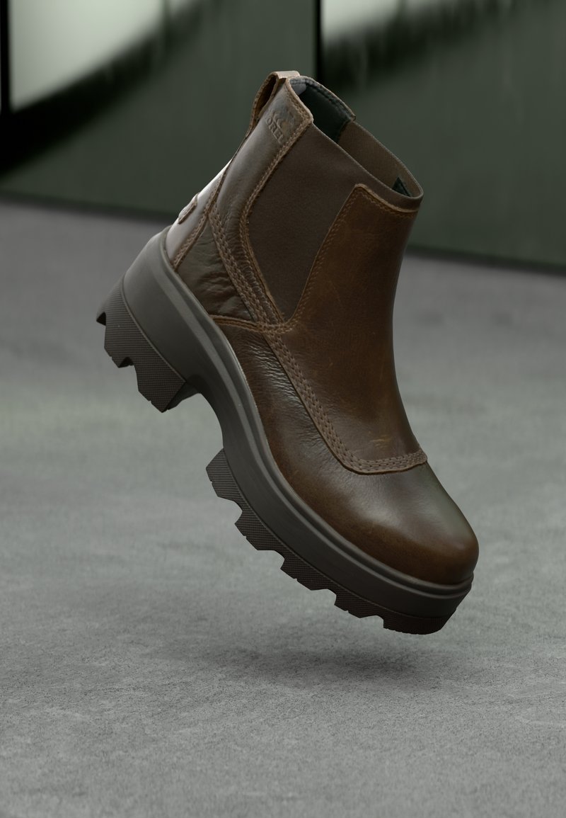 Bottines en cuir marron avec une finition texturée, dotées d'une semelle en caoutchouc noir épais avec un motif de traction et un détail de languette.