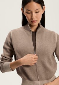 Bežna zip-up pulover s visokim ovratnikom, rebrastimi manšetami in pasom, ki se ponaša z gladko teksturo in prilegajočim dizajnom.