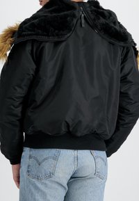 Sort bomberjakke med faux fur krave, lynlås bagpå, ribbede ærmer og kant, samt en struktureret overflade, parret med lyseblå jeans.