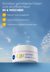 White round cream jar with a lavender band, labeled "Q10 Anti-Falten Beruhigung," featuring a blue logo and ingredient details against a blue sky.
