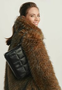 Czarna skórzana torba o pikowanym wzorze, z płaskim kształtem i gładką teksturą, noszona na brązowym futrze z puszystym wykończeniem.