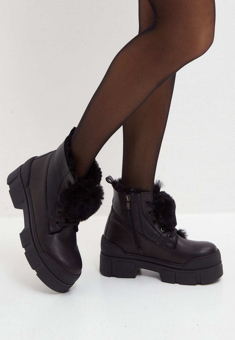 Botas de tobillo negras hechas de cuero suave con forro de piel sintética, suela gruesa, cordones en la parte delantera y cremallera lateral.
