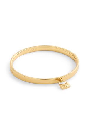 Bracelet jonc en tome dorée avec des bords lisses et arrondis, arborant un petit charme en forme de sac à main. Design épuré, finition brillante.