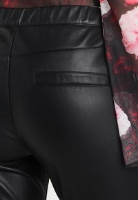 Black faux leather pants with a back pocket detail, paired with a sheer floral blouse featuring red and white patterns.