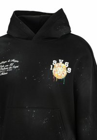 Schwarzer Hoodie aus Baumwolle, ausgestattet mit einer Fronttasche, Spritzmuster, gesticktem Löwenmotiv in lebendigen Farben und weißen Textelementen.