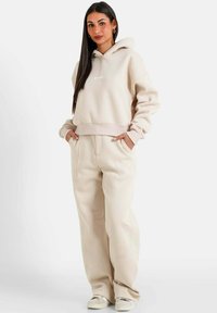 Beige sweatshirt met een capuchon en een voorzak, met ribgebreide onderrand. Gepaarde met bijpassende wijde broek van zacht, textuurachtig stof.