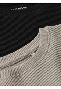 Dvě pletené crewneck trika poskládaná na sobě, jedno černé a jedno světle béžové. Obě mají texturovanou látku a viditelné švy kolem výstřihu.