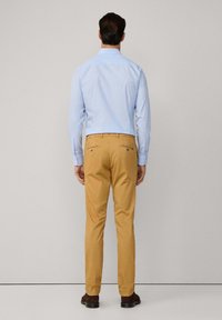 Camicia azzurra chiara con bottoni e pantaloni slim-fit beige. La camicia ha maniche lunghe e i pantaloni presentano due tasche posteriori con bottoni. Tessuto morbido al tatto.