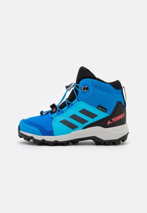 Zapato de senderismo azul y negro con un diseño de tobillo alto, parte superior de textil, suela de goma negra y tres franjas oscuras notables en el lateral.