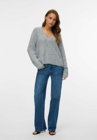 Hall kujuline hall kašmiirsweater V-kaelusega ja vabalt istuv, koos kõrge vöökohaga siniste laienevate teksade ja mustade avatud varvate kontsakingadega.