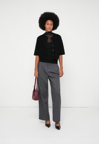Black short-sleeve cardigan with buttons, worn over a black top; paired with light gray wide-leg trousers and black pointed-toe heels. Maroon handbag.