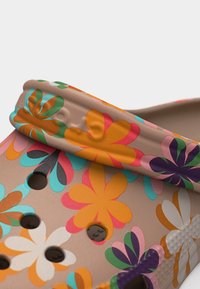 Μπεζ παπούτσι τύπου κλογκ με πολύχρωμο λουλουδάτο σχέδιο, τρύπες αερισμού και υφασμένο λουράκι στη φτέρνα.