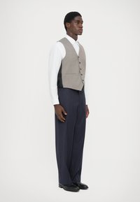 Vest gri peste o cămașă albă, asortat cu pantaloni navy cu dungi subțiri. Caracteristici remarcabile includ o croială ajustată și texturi netede.